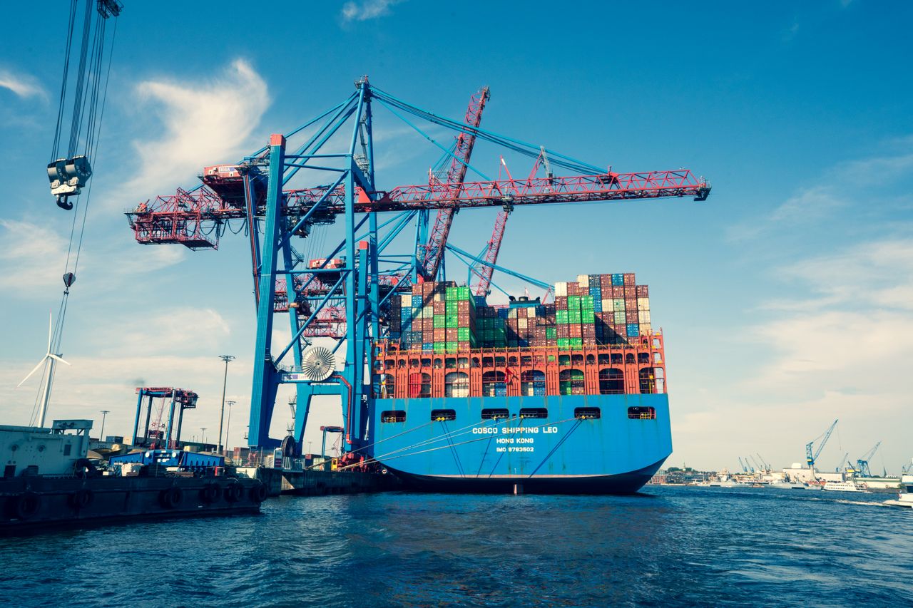 hero-img-02 A vibrant scene of a bustling shipping port with towering cranes and a large container ship.