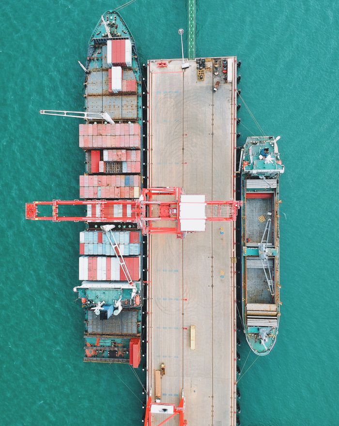 services-01 Aerial shot of cargo ships docked at a harbor with cranes and containers.